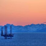 Emergency Barrels Vanish — What’s Coming? An oil rig in the ocean with a backdrop of mountains during sunset
