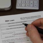 Hand filling out an SBA loan application form on a desk