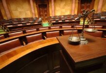 A courtroom with empty seats and a scale of justice in the foreground