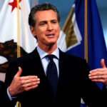 Money Trails Shadow California’s First Couple Man speaking with flags in the background
