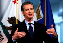 Money Trails Shadow California’s First Couple Man speaking with flags in the background