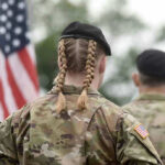 Soldier with braided hair in uniform, American flag visible.