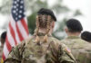 Soldier with braided hair in uniform, American flag visible.
