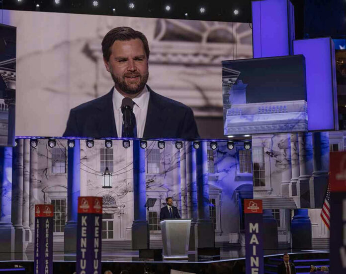 Man speaking at podium on stage, projection behind him.