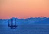 Trump Threatens to Seize Iran’s Oil Hubs — Gas Prices Already Above $100 An oil rig in the ocean with a backdrop of mountains during sunset