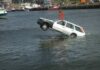 A white car being lifted out of the water by a crane at a port