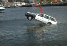 A white car being lifted out of the water by a crane at a port