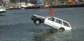 A white car being lifted out of the water by a crane at a port