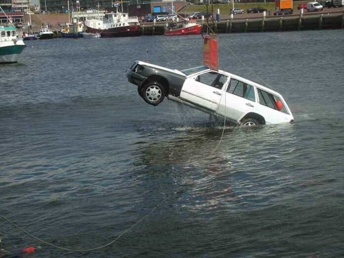 A white car being lifted out of the water by a crane at a port