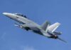 Twin-engine fighter jet climbing in a clear blue sky