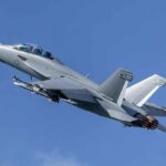 Twin-engine fighter jet climbing in a clear blue sky