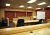 Medical Gray Zone On Trial Interior view of an empty courtroom with wooden furniture and American flags