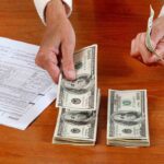Billionaires Tax Bombshell—What’s Next? Hands counting cash and reviewing financial documents on a wooden table