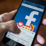 Hand using smartphone with Facebook reactions on screen