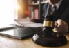 Judge's gavel on desk with person reading documents in background