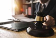 Judge's gavel on desk with person reading documents in background