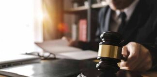 Judge's gavel on desk with person reading documents in background