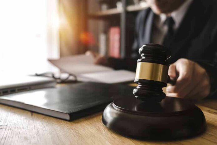 Judge's gavel on desk with person reading documents in background