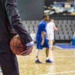Basketball coach in suit holding ball courtside