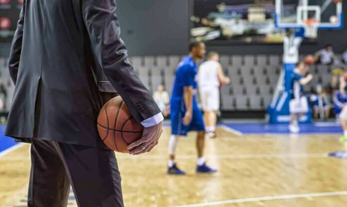 shutterstock_1089242369-1 Basketball coach in suit holding ball courtside