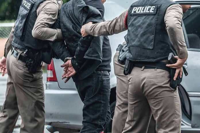 Police officers arresting a person beside a car