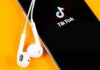 Smartphone with TikTok app and white wired earbuds on yellow background