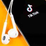 Smartphone with TikTok app and white wired earbuds on yellow background