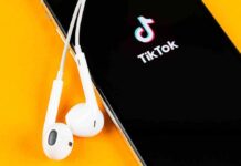 Smartphone with TikTok app and white wired earbuds on yellow background