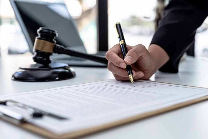 shutterstock_2103308165 Hand signing legal document beside gavel and laptop