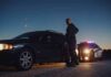 Police officer stands beside a stopped car at dusk