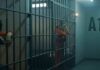 prison cell with inmates in orange jumpsuits behind bars