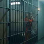 prison cell with inmates in orange jumpsuits behind bars