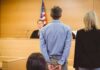 Defendant in handcuffs stands before a judge in a courtroom