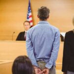 Defendant in handcuffs stands before a judge in a courtroom