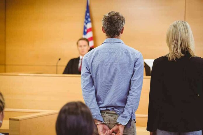 Defendant in handcuffs stands before a judge in a courtroom
