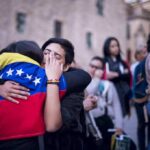 Two people hug tightly, one draped in a Venezuelan flag, amid a crowd