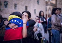Due Process Theater Masks Brutal Reality Two people hug tightly, one draped in a Venezuelan flag, amid a crowd