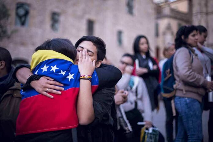 shutterstock_625973180 Two people hug tightly, one draped in a Venezuelan flag, amid a crowd