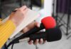Amazon Jet Disaster Slams Miami Journalist holding two microphones while writing in a notebook