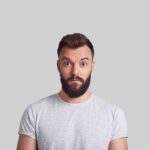 Man with beard making surprised face against gray background