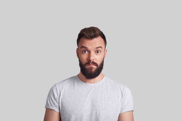 shutterstock_1011188638 Man with beard making surprised face against gray background