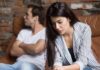 woman looking down while man sits with arms crossed on couch