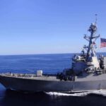 Naval destroyer sailing on open sea with flag flying