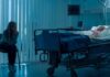 hospital room with child in bed and adult sitting nearby