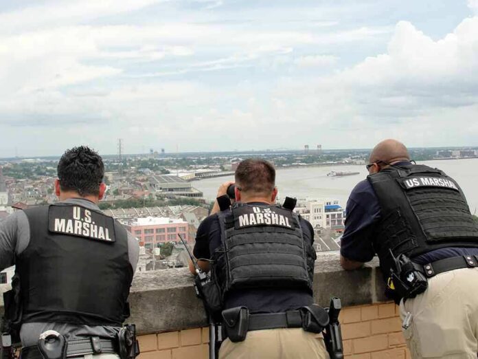 Three U.S. Marshals in tactical vests overlooking a city and river
