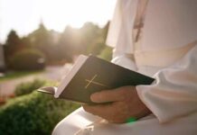Person in white robe holding a Bible outdoors