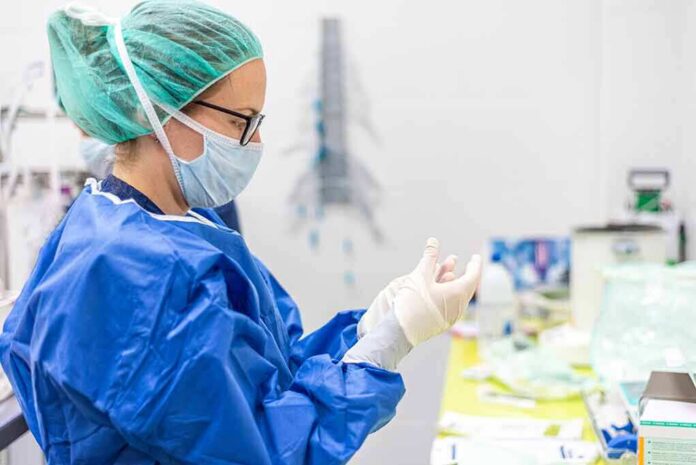 medical professional in blue gown putting on sterile gloves
