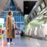 Woman with yellow suitcase wearing mask at airport check-in area