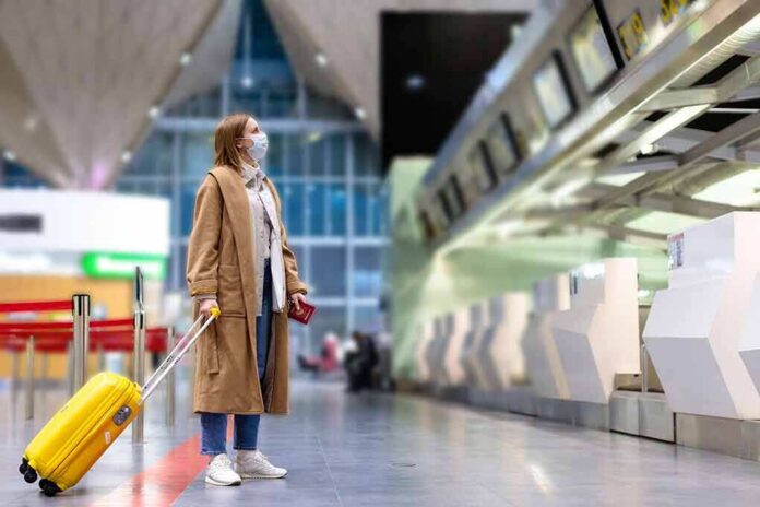 shutterstock_1681005856 Woman with yellow suitcase wearing mask at airport check-in area