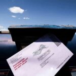 Mail-in ballot being inserted into a blue USPS mailbox